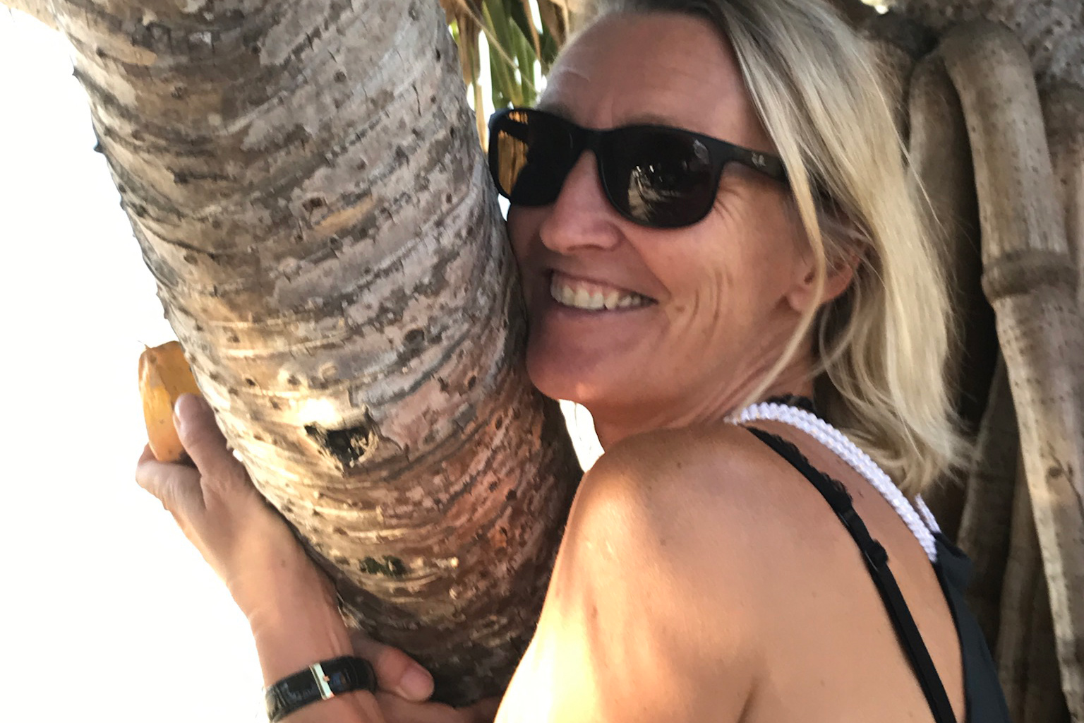 Dorthe Broeng med solbriller læner sig smilende op ad en træstamme