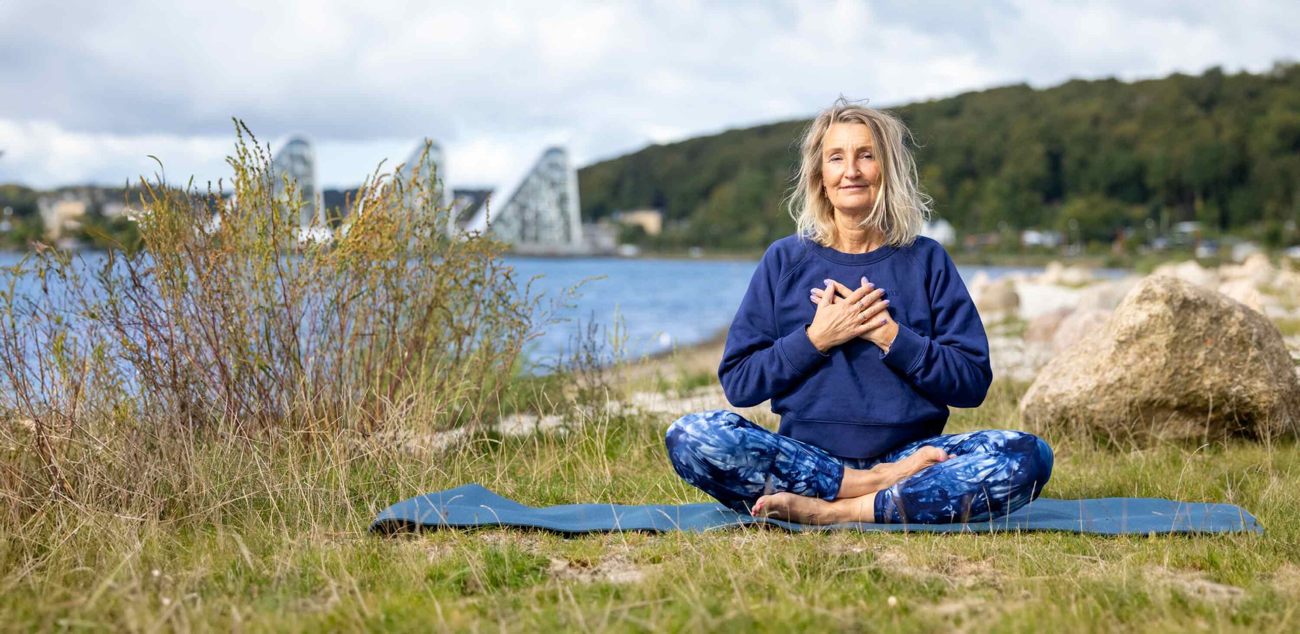 Dorthe Broeng sidder i meditation på en måtte ved fjorden